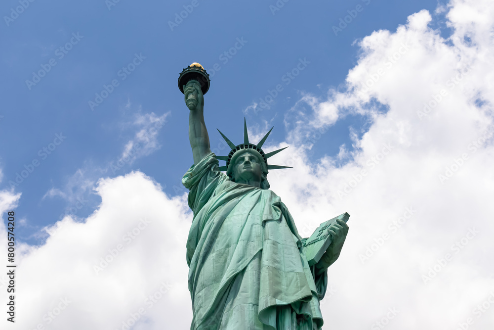 Fototapeta premium A close up on an iconic representation of freedom and independence, the Statue of Liberty with flaming torch on Liberty Island. The Lady on a Pedestal is surrounded by clouds. American history.