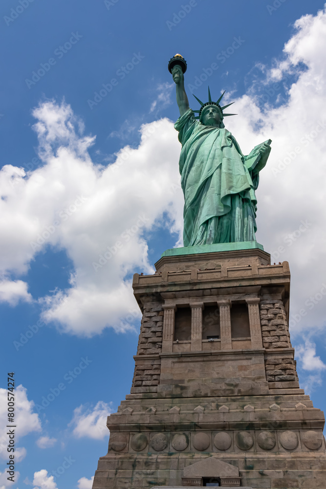 Fototapeta premium A close up on an iconic representation of freedom and independence, the Statue of Liberty with flaming torch on Liberty Island. The Lady on a Pedestal is surrounded by clouds. American history.