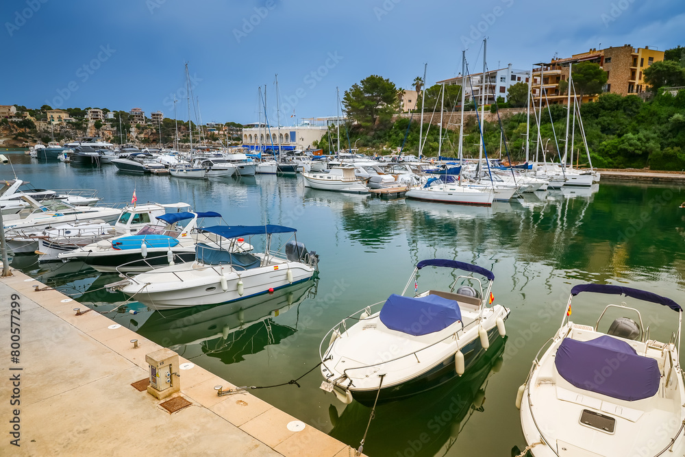 Obraz premium The Porto Cristo harbor in Mallorca offers a serene scene with boats gently anchored amidst a backdrop of coastal buildings