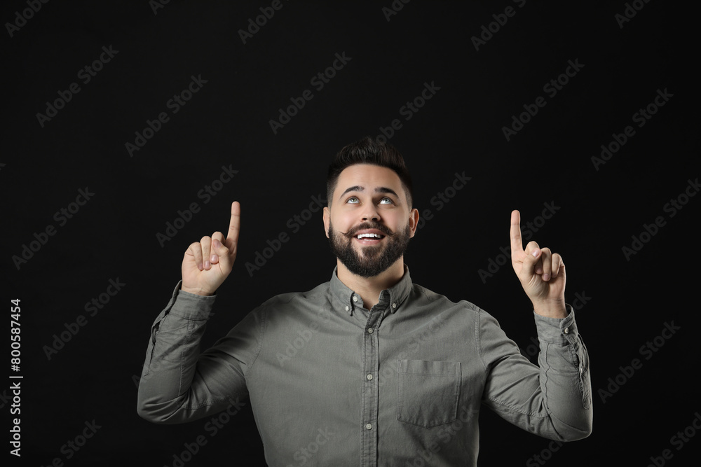 Young man with mustache pointing at something on black background. Space for text Young man with mustache pointing at something on black background. Space for text
