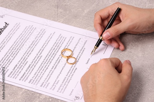 Man signing marriage contract at light grey table, closeup