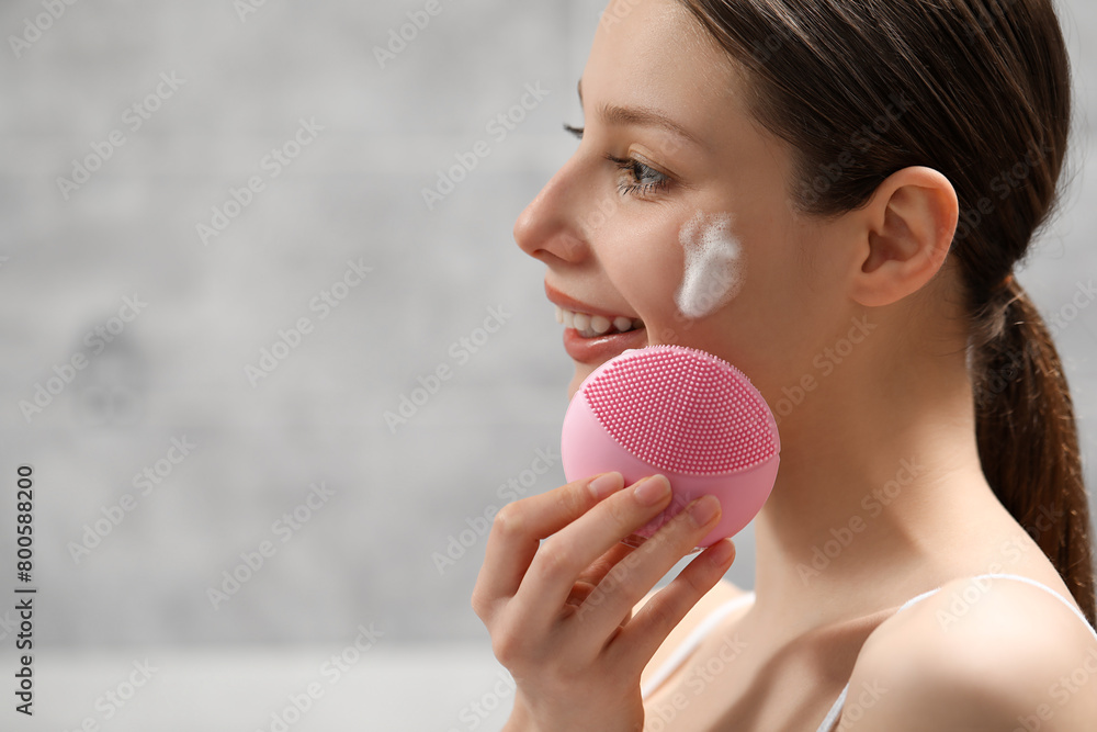 Young woman washing face with brush and cleansing foam indoors. Space for text Young woman washing face with brush and cleansing foam indoors. Space for text