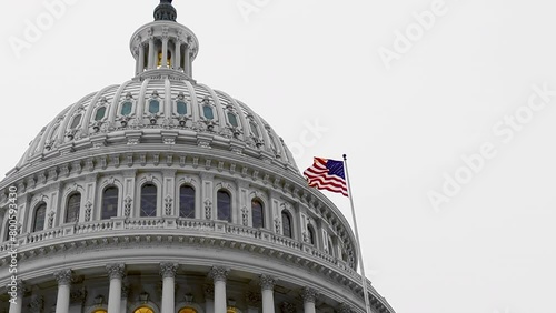 Low angle lockdown shot of American flag waving and capitol building against clear sky