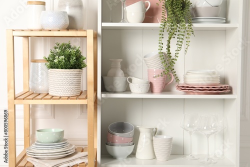 Different clean dishware and houseplants on shelves in cabinet indoors