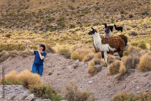 A woman takes a selfie against the background of llamas.