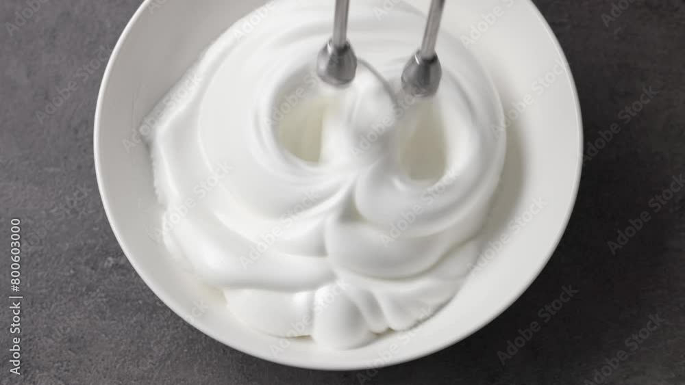 Chef whips raw egg whites with powdered sugar in a white bowl with a mixer, top view. Close-up of food Chef whips raw egg whites with powdered sugar in a white bowl with a mixer, top view. Close-up of food