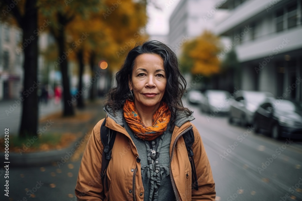 A woman wearing a brown coat and orange scarf stands on a street A woman wearing a brown coat and orange scarf stands on a street