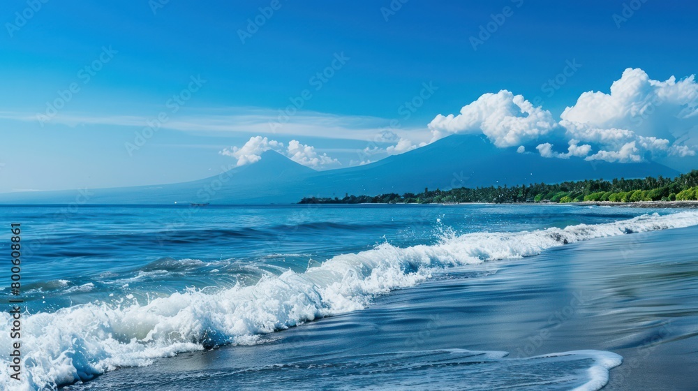 Pristine white-sand beach with gentle waves lapping on the shore, and a majestic mountain range looming in the distance under a clear blue sky