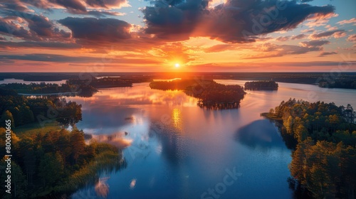 The sun sets in a blaze of glory over a large lake dotted with islands and surrounded by forests