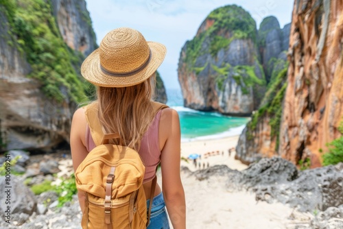 A woman in a straw hat and with a backpack over her shoulders stands on a rocky beach between two rocks, viewed from the back. © Neuraldesign