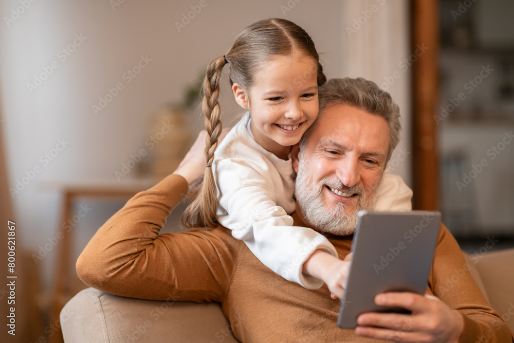 Man and Little Girl Sitting on Couch Viewing Tablet