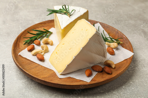Plate with pieces of tasty camembert cheese, nuts and rosemary on grey textured table, closeup