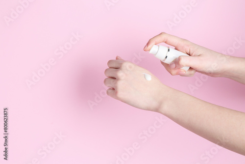 Woman applying cream on her hand against pink background, closeup. Space for text © New Africa