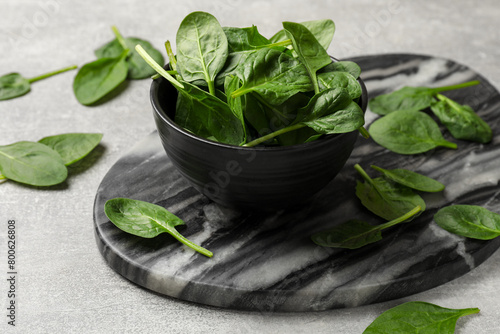 Fresh spinach leaves in bowl on light textured table  closeup