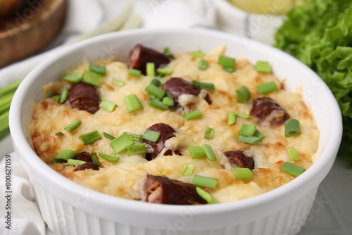 Tasty sausage casserole with green onion in baking dish on white table, closeup