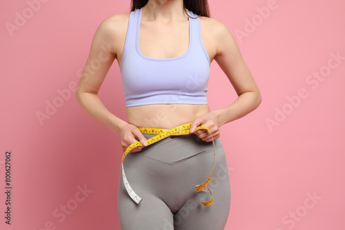 Woman with measuring tape showing her slim body on pink background, closeup