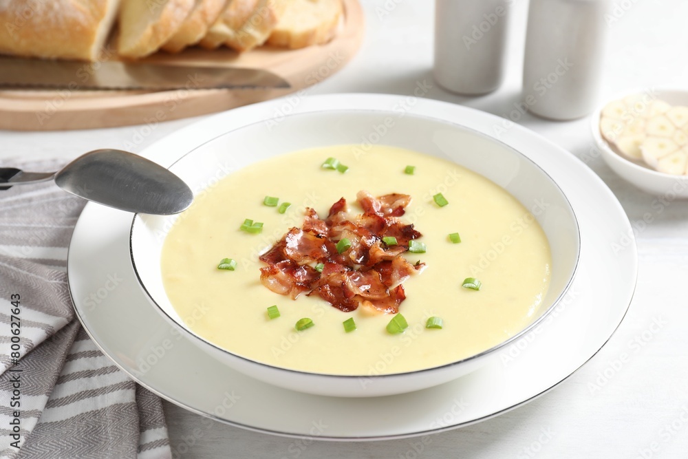 Tasty potato soup with bacon in bowl and spoon on white table