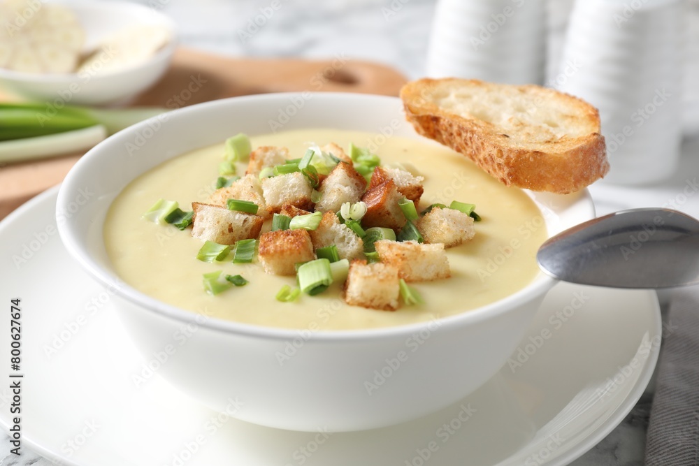 Tasty potato soup with croutons in bowl and spoon on white table Tasty potato soup with croutons in bowl and spoon on white table