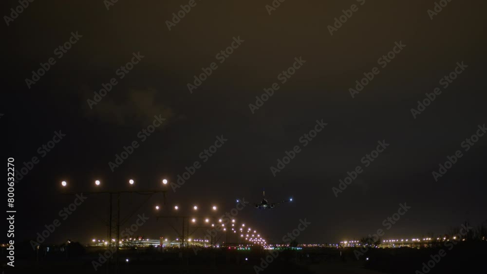 Airplane with red tail and blue wing lights descending towards a curving runway of bright lights at night Airplane with red tail and blue wing lights descending towards a curving runway of bright lights at night