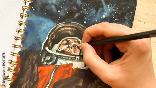 CLose-up view of hand drawing cosmonaut in outer space in sketchbook. Astronaut illustration. Sketching dreams. Aquarelle painting album. Film grain texture. Soft focus. Blur