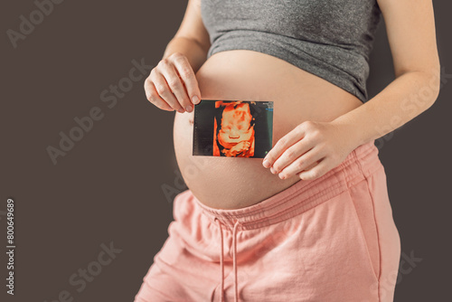Expectant mother tenderly connects with her unborn child, holding ultrasound photo to her pregnant belly photo