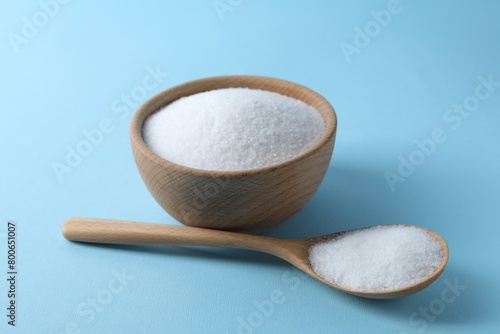 Organic white salt in bowl and spoon on light blue background