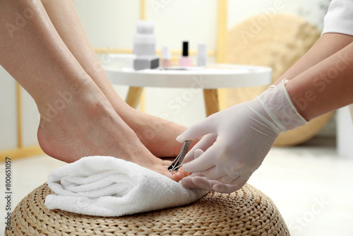 Professional pedicurist cutting client`s toenails with clipper in beauty salon, closeup