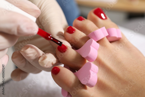 Pedicurist painting client s toenails with red polish in beauty salon  closeup