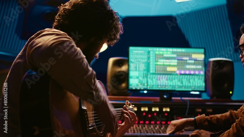 Young artist songwriter composing a new song on guitar in recording session at studio, creating tunes and editing them after in post production. Musician composer producing tracks. Camera B.