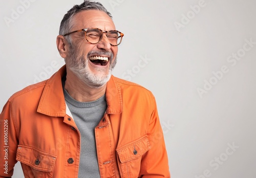 a happy middleaged man with glasses wearing an orange jacket and gray t-shirt laughs against a white background © IgnacioJulian