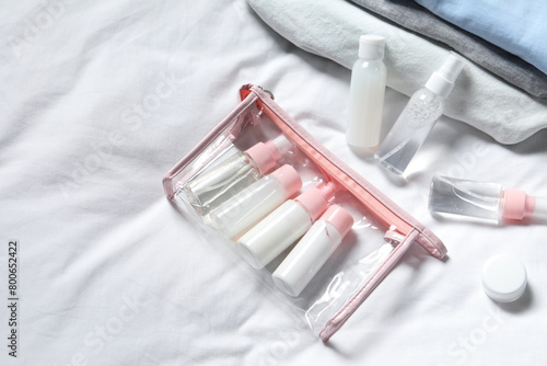 Cosmetic travel kit. Plastic bag with small containers of personal care products on bed, above view