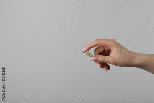 Woman holding vitamin capsule on grey background, closeup with space for text. Health supplement
