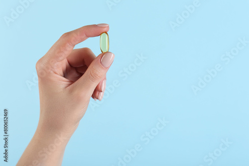 Woman holding vitamin capsule on light blue background, closeup with space for text. Health supplement