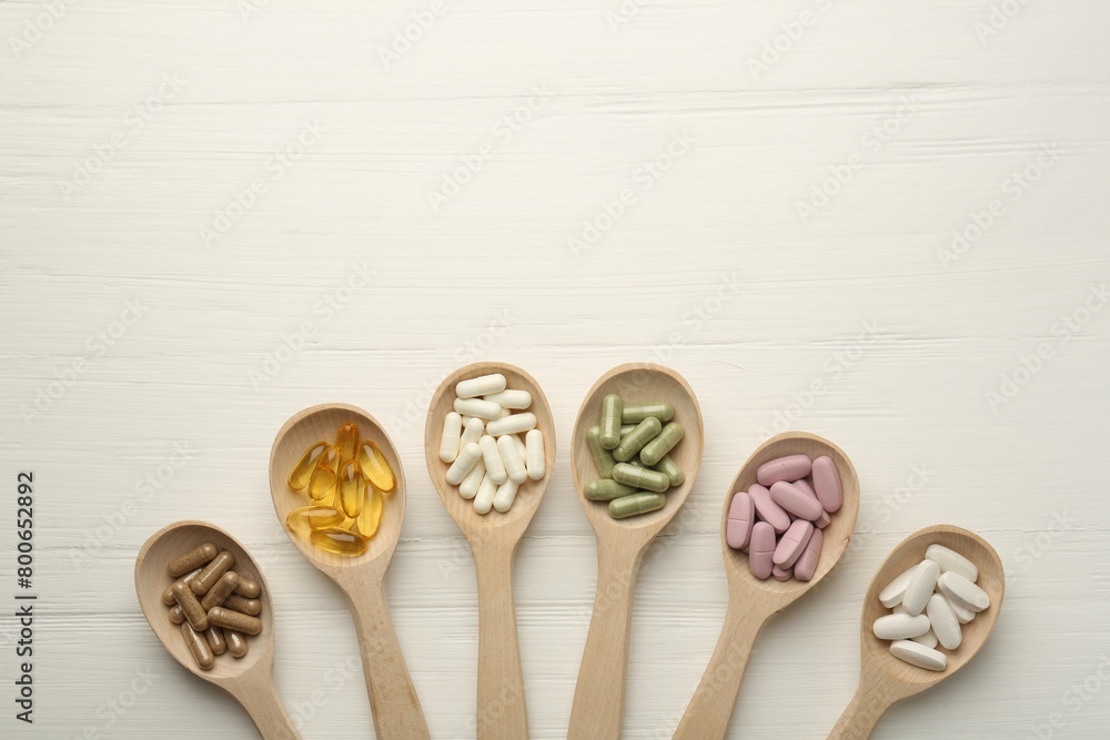 Different vitamin capsules in spoons on white wooden table, flat lay. Space for text Different vitamin capsules in spoons on white wooden table, flat lay. Space for text