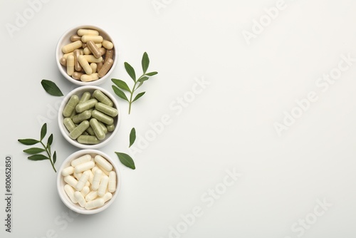 Cuadro en lienzo Different vitamin capsules in bowls and leaves on white background, flat lay