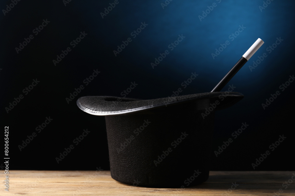 Magician's hat and wand on wooden table against dark background Magician's hat and wand on wooden table against dark background