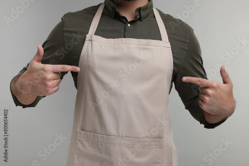 Fotografie Man pointing at kitchen apron on grey background, closeup