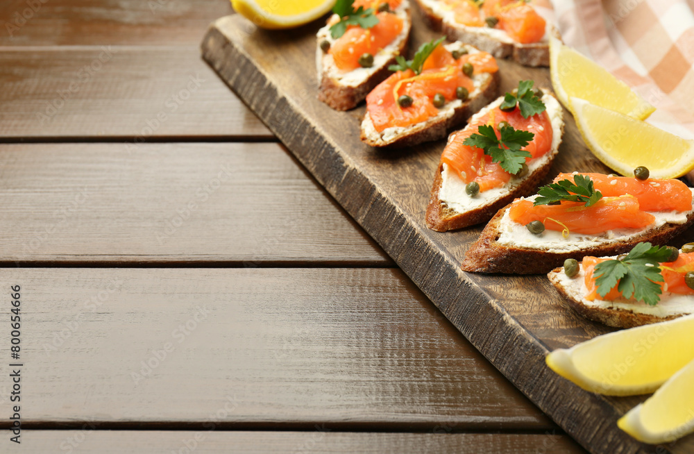 Tasty canapes with salmon, capers, lemon and cream cheese on wooden table, closeup. Space for text