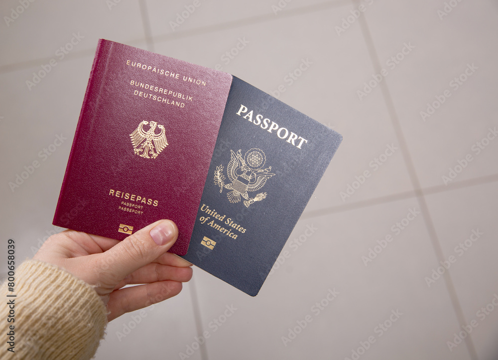 Close up of a female hand holding a German and an American passport Close up of a female hand holding a German and an American passport