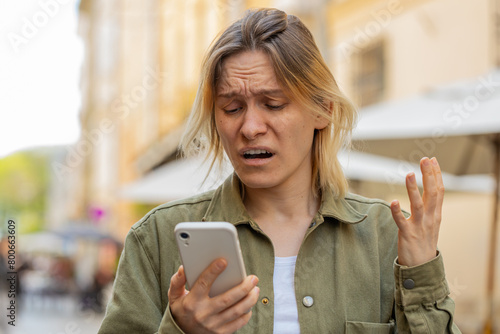 Caucasian young woman using smartphone typing browsing loses becoming surprised sudden lottery results bad news fortune loss app fail virus thief fraud outdoors. Tourist girl on urban city street.