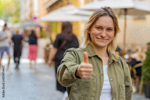Like. Happy pretty young woman looking approvingly at camera showing thumbs up like sign positive something good positive feedback. Excited Girl celebrate success on city street. Town lifestyles.
