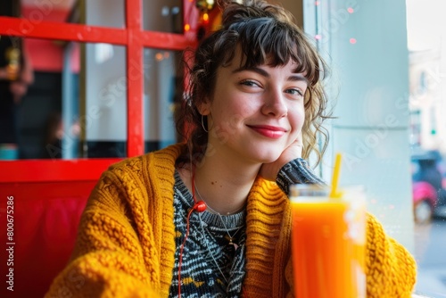 Happy young student sits cozily in a vibrant cafe, enjoying a fresh glass of orange juice, exuding warmth and contentment in a casual, urban setting © Minerva Studio