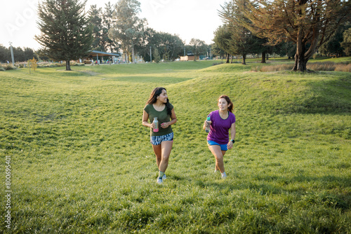 Fitness Friends: Two Latin Women Walking on the grass in the Park after running exercise at sunset.