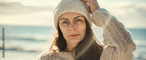 Mature brunette woman wearing knit sweater at beach coast on cold sunny day