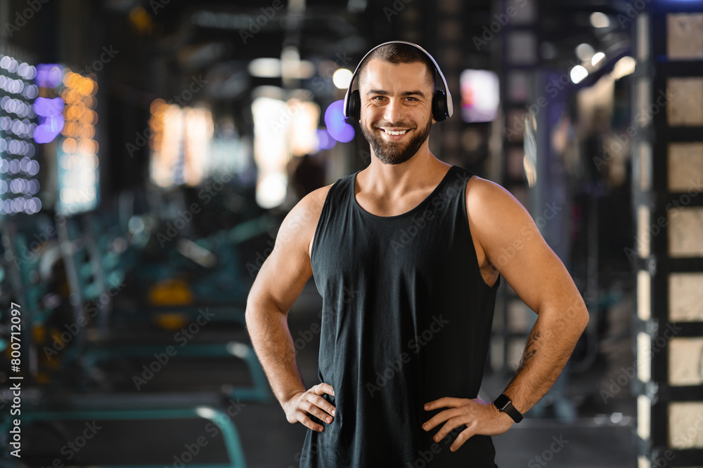 Handsome Millennial Man With Headphones Standing in Gym