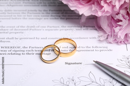 Marriage contract, golden wedding rings, pen and flowers, closeup