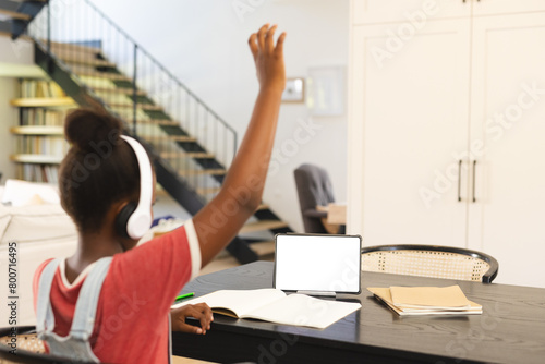 African American girl in headphones raises hand in tablet-based online lesson, copy space