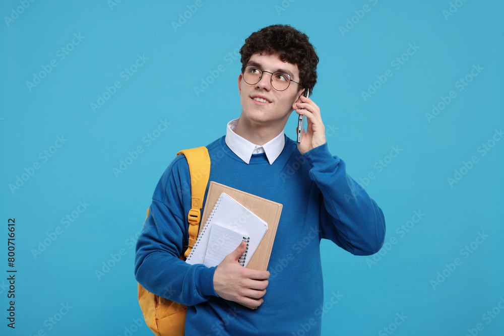 Portrait of student with backpack and notebooks talking on smartphone against light blue background Portrait of student with backpack and notebooks talking on smartphone against light blue background