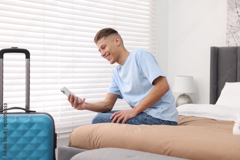 Smiling guest with smartphone on bed in stylish hotel room Smiling guest with smartphone on bed in stylish hotel room