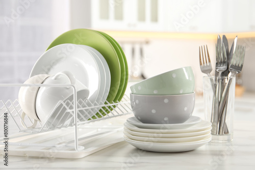 Many different clean dishware, cups and cutlery on white marble table in kitchen